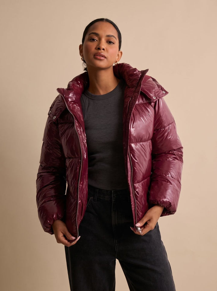 Damen-Steppjacke mit glänzender Oberfläche und Kapuze, frontal vor neutralem Hintergrund